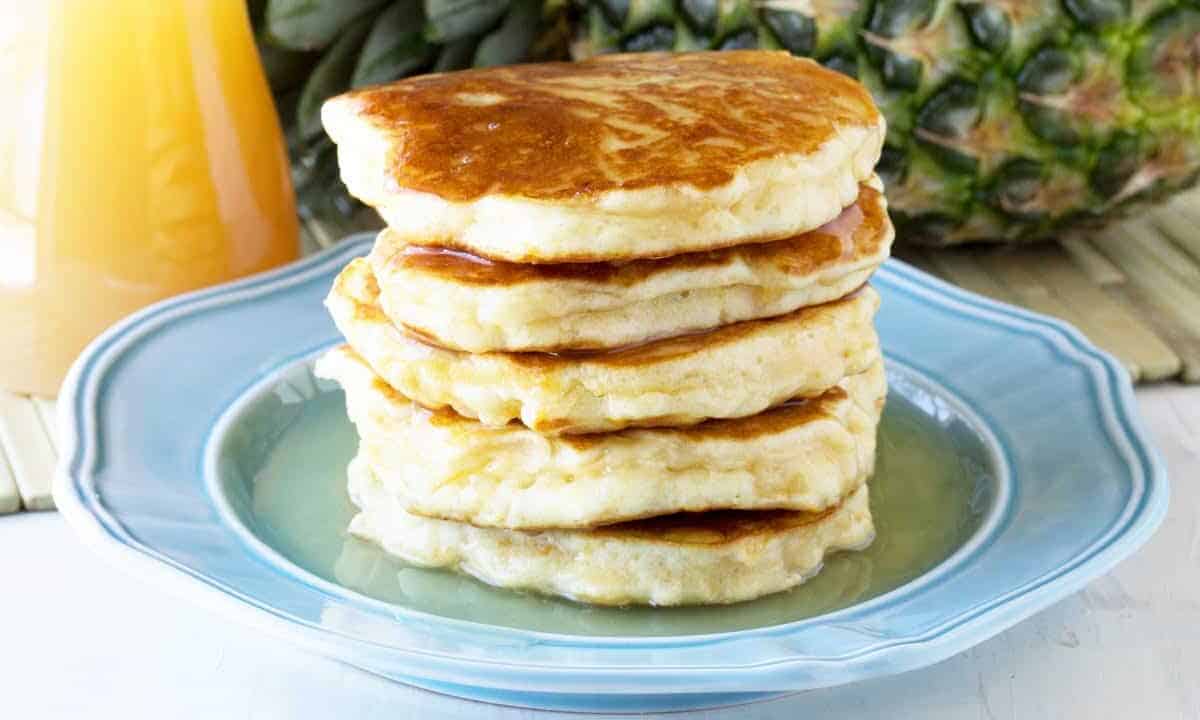 Angled view of a stack of Pineapple Pancakes on a decorative light blue plate drizzled with Coconut Syrup.