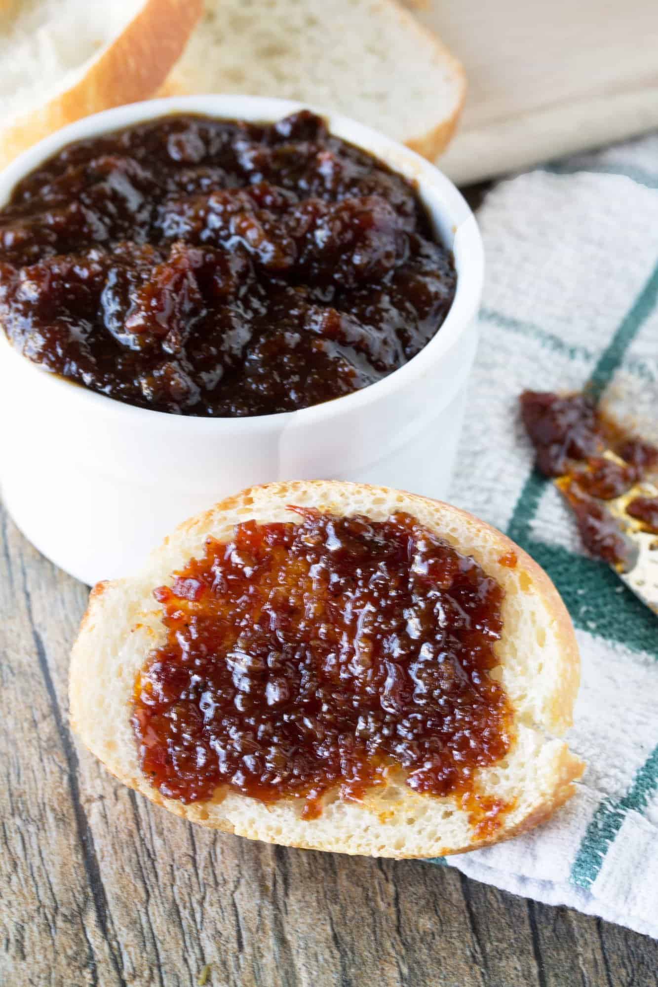 Bacon jam on a slice of bread with a bowl of bacon jam in the background.