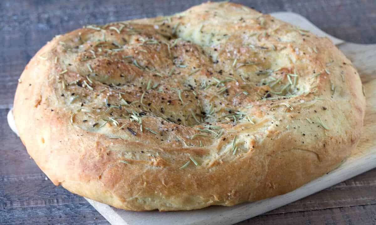 Angled view of Easy Homemade Rosemary Focaccia on a wood cutting board.