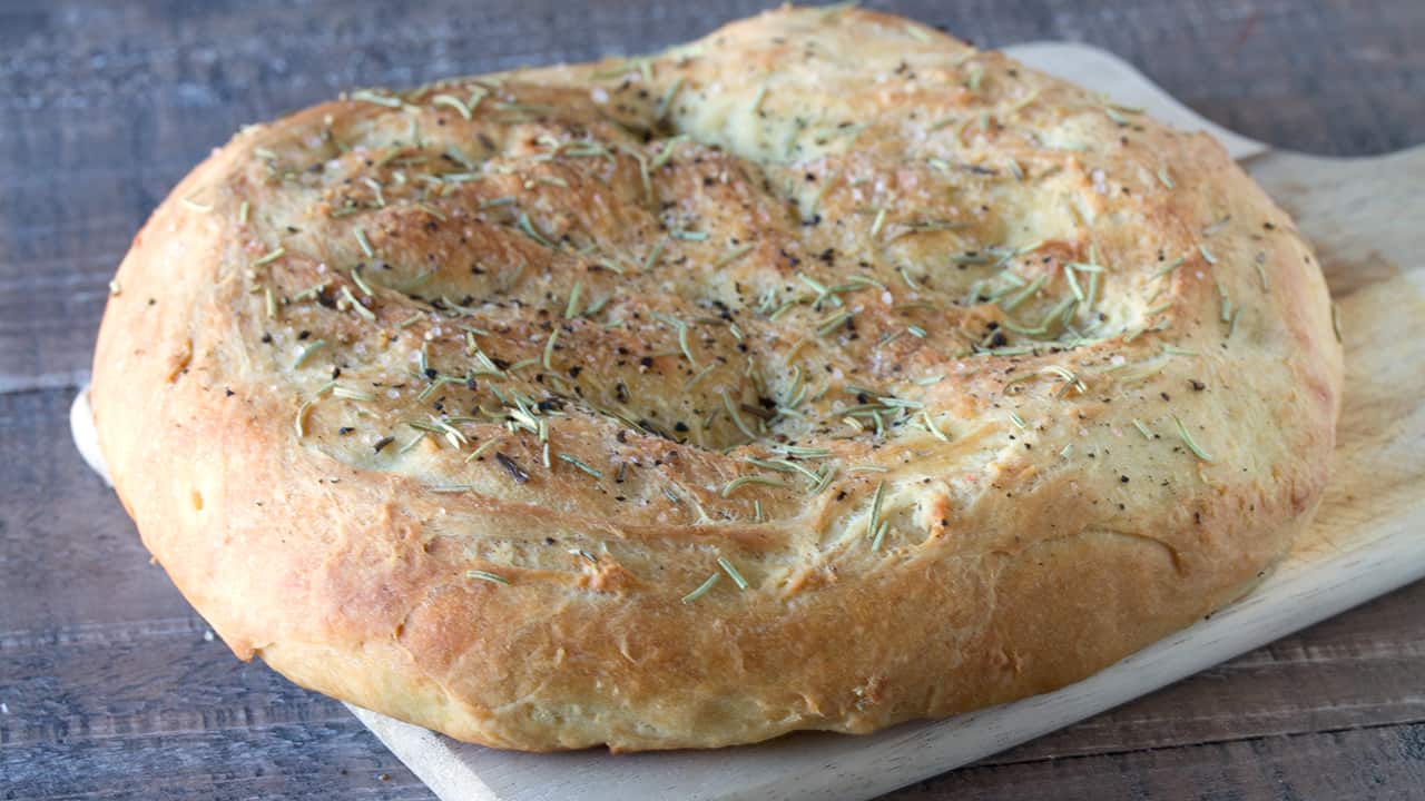 Angled view of Easy Homemade Rosemary Focaccia on a wood cutting board.