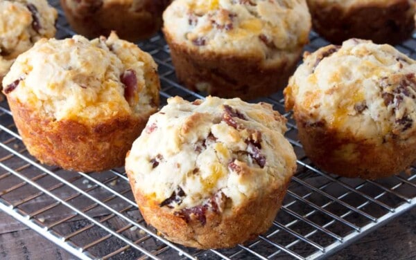 A hand is holding up a Bacon Cheddar Muffin with the rest on a cooling rack in the background.