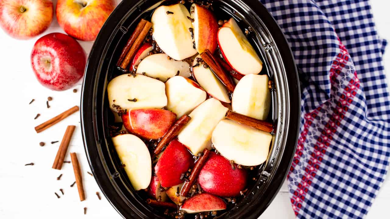 Bird's eye view of a slow cooker full of Apple Cider made from scratch with floating rough cut apples and sticks of cinnamon.