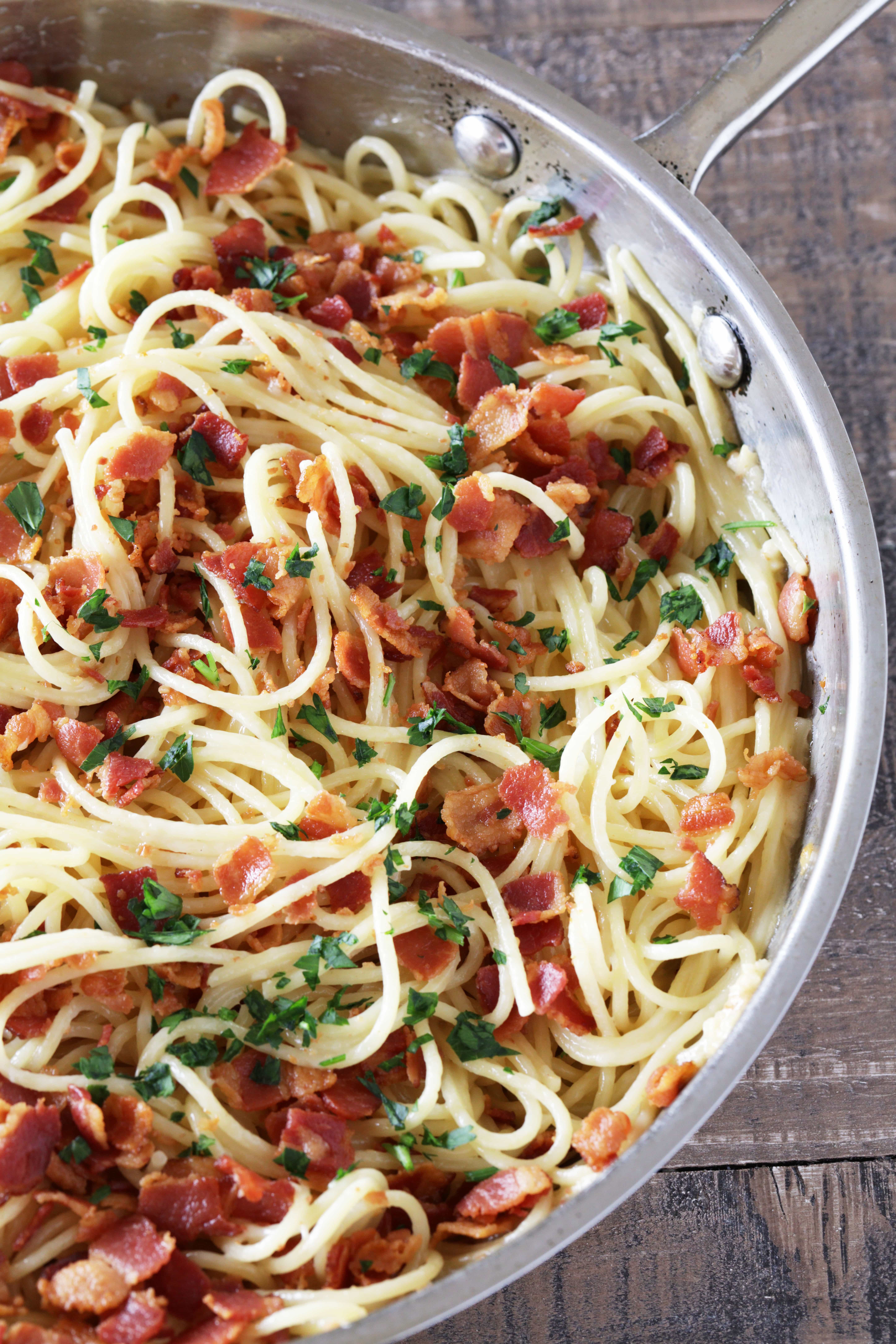 Eggless Spaghetti Carbonara with rich flavor from bacon and garlic and its creamy texture from parmesan cheese and cream. Sprinkled with freshly chopped parsley in a skillet.