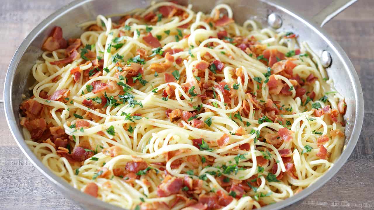 Angled view of Eggless Spaghetti Carbonara in a sauce pan garnished with bacon and parsley.