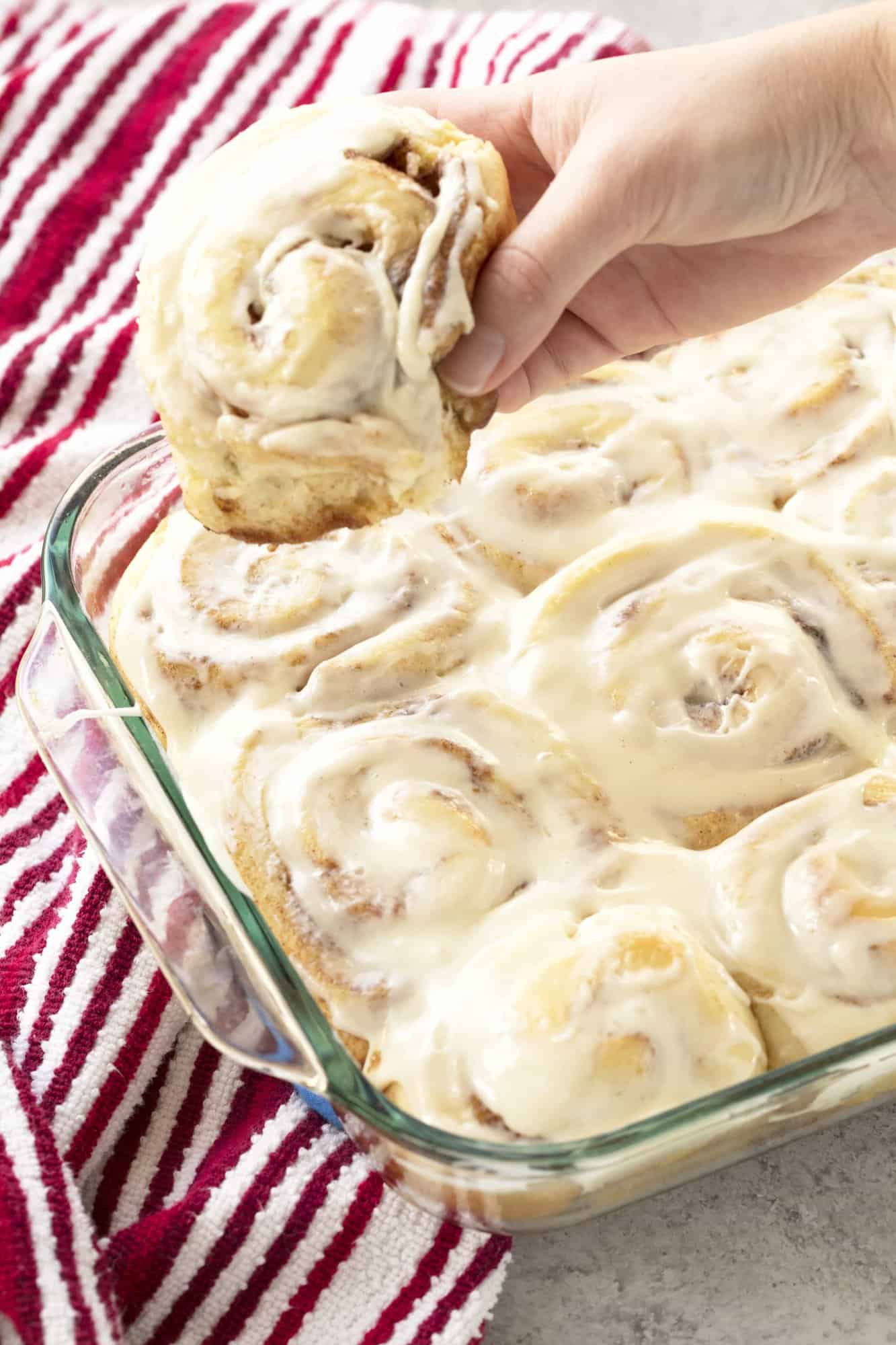 A Homemade glazed Cinnamon Roll is taken from the pan.