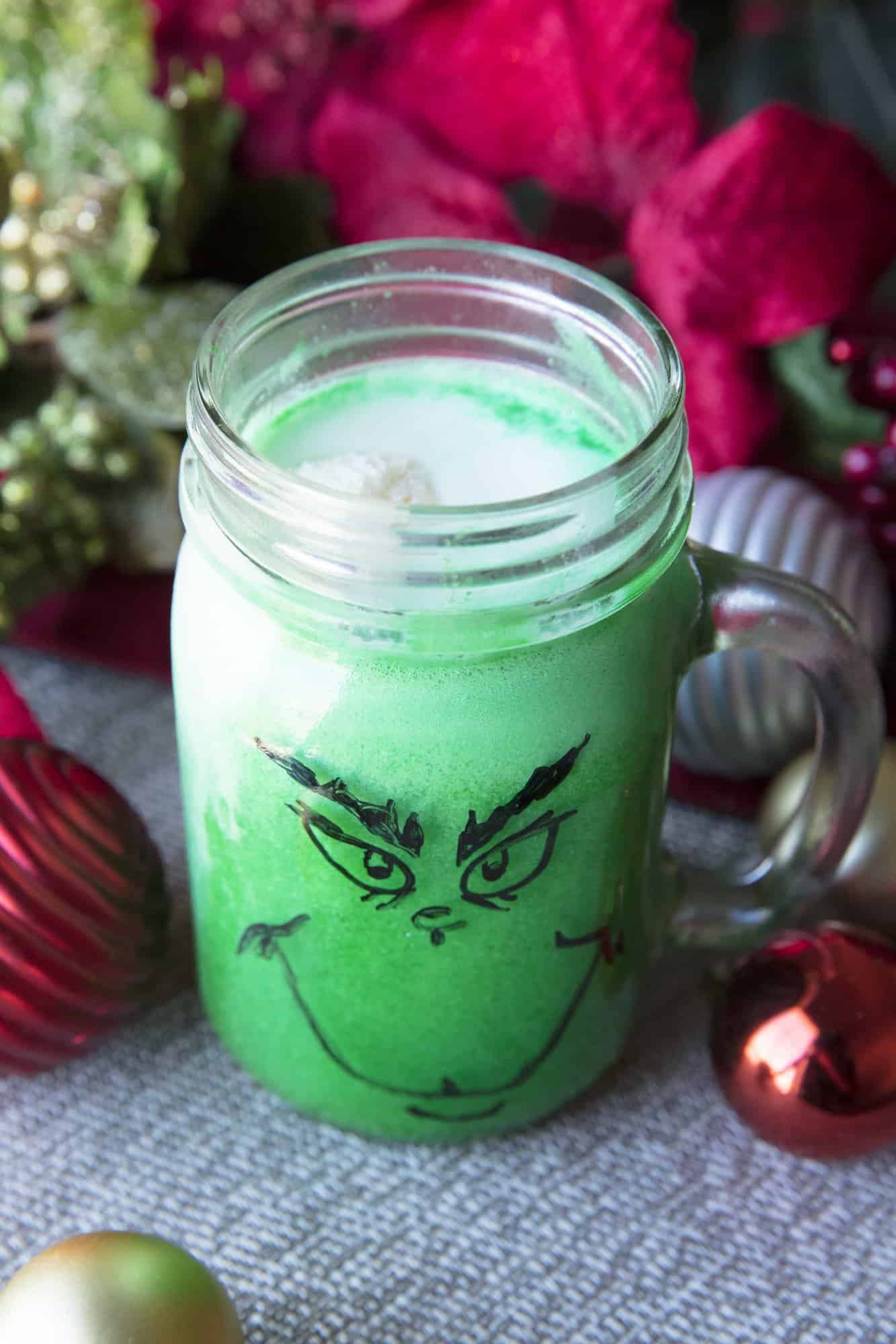 Green grinch punch in a mason jar cup with a handle and a grinch face drawn on it with a marker