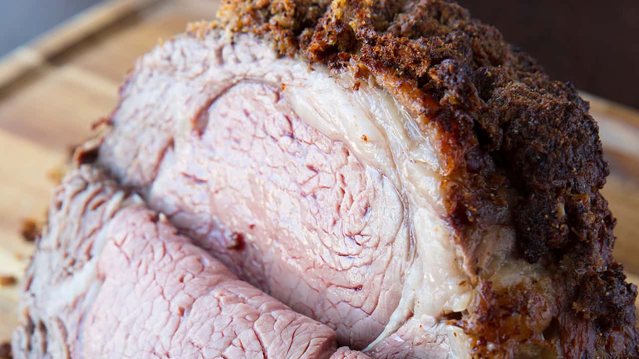 Close-up view of Prime Rib Roast with a slice in it to show juiciness on a wood cutting board.