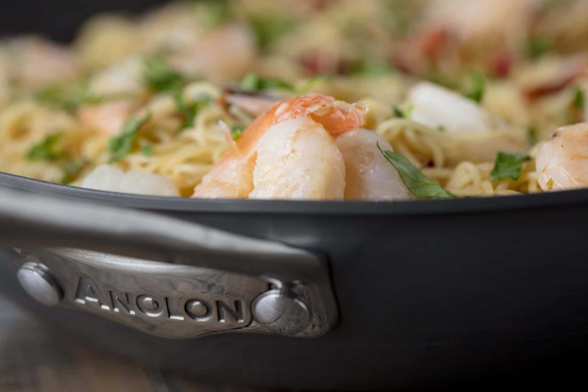 Close up of a cooking pan full of Tomato Shrimp Angel Hair Pasta to show the Anolon logo on the side.