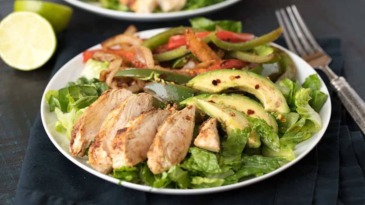 Angled view of Skinny Chicken Fajita Salad on a white dinner plate setting on a dark cloth table napkin.