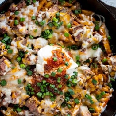Bird's eye view of Steak and Potato Nachos garnished with sour cream, green onions, and drizzled with hot sauce all in a skillet.
