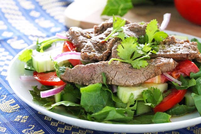 Angled view of Thai Beef Salad served on a white dish and placed on a blue decorative towel.