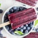 Blueberry and basil popsicle over a bowl full of blueberries.