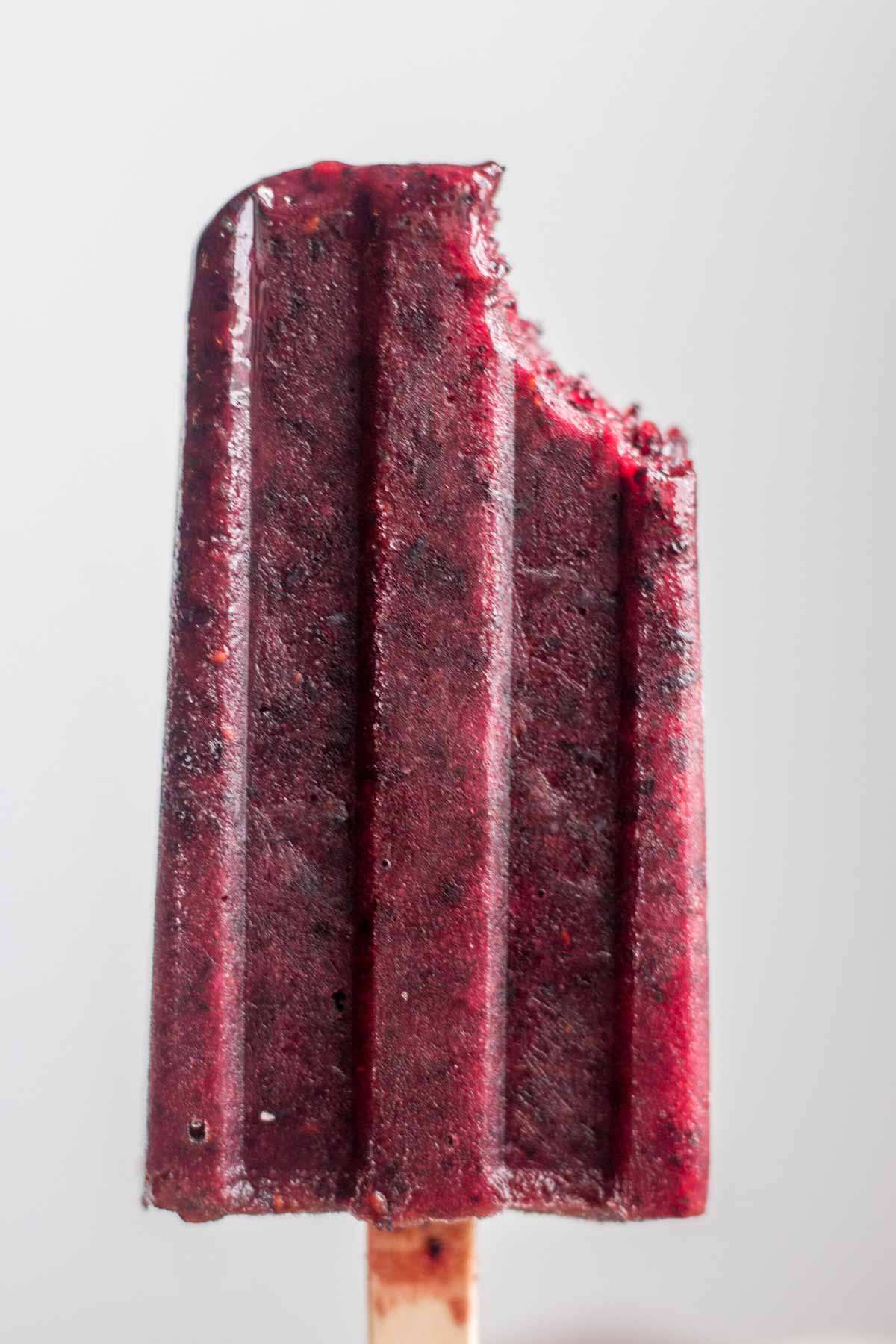 Close up of a blueberry and basil popsicle with a bite taken out of it. 