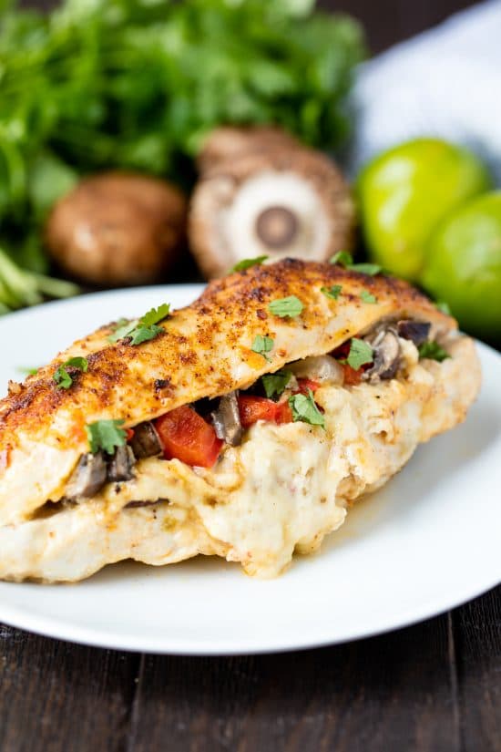 Fajita stuffed chicken breast on a white plate with mushrooms, peppers, and cheese.