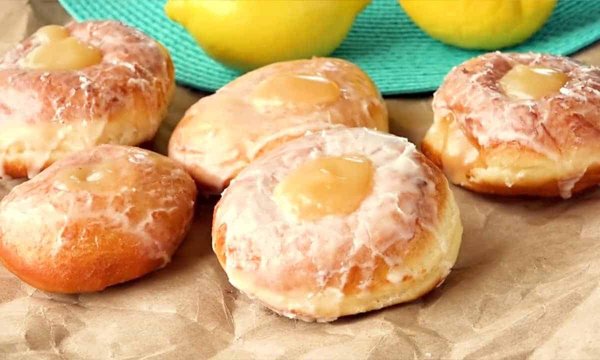 Close up of a Lemon Filled Doughnut on brown paper with fresh lemons in the background.