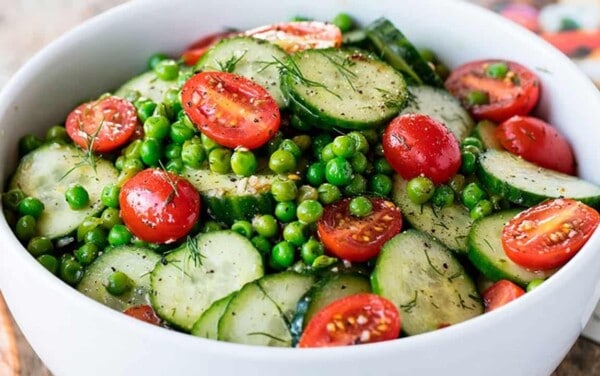 Close-up view of Dill Pea and Cucumber Salad in a white bowl garnished with halved cherry tomatoes.