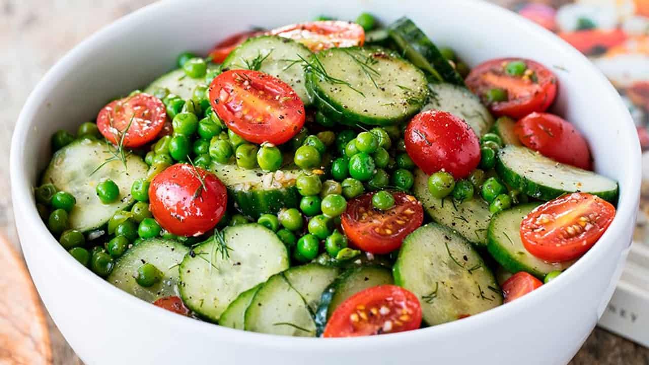 Close-up view of Dill Pea and Cucumber Salad in a white bowl garnished with halved cherry tomatoes.
