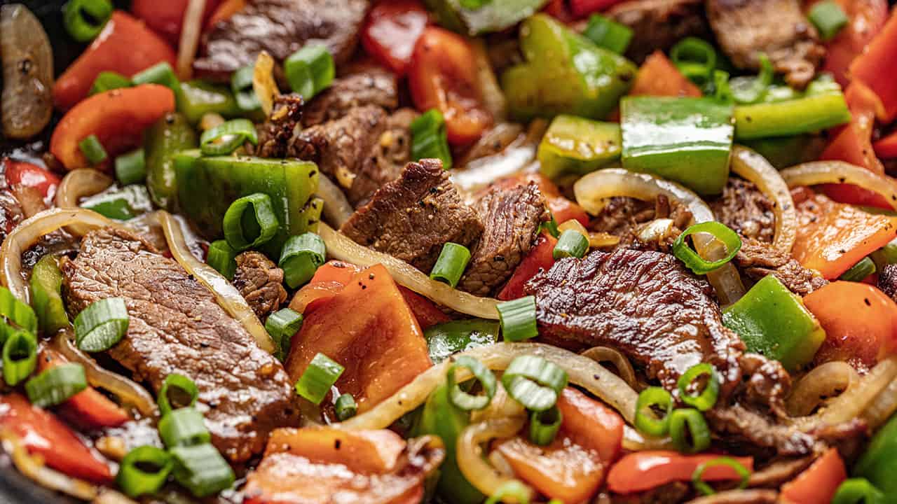 Closeup of Easy Chinese Pepper Steak with red and green peppers, white onion and chopped green onion