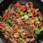 Easy Chinese Pepper Steak in a skillet with steak, red and green peppers, white onion and chopped green onion