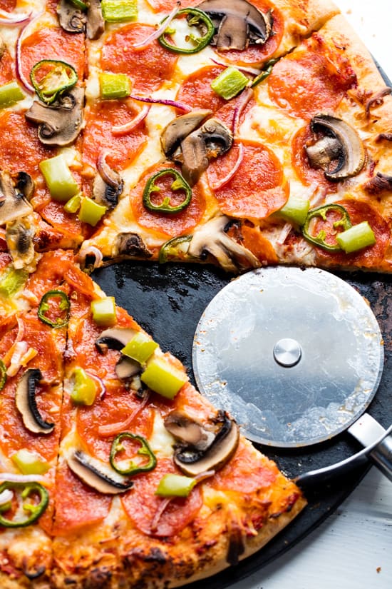 Baked homemade frozen pizza with a slice removed and pizza cutter