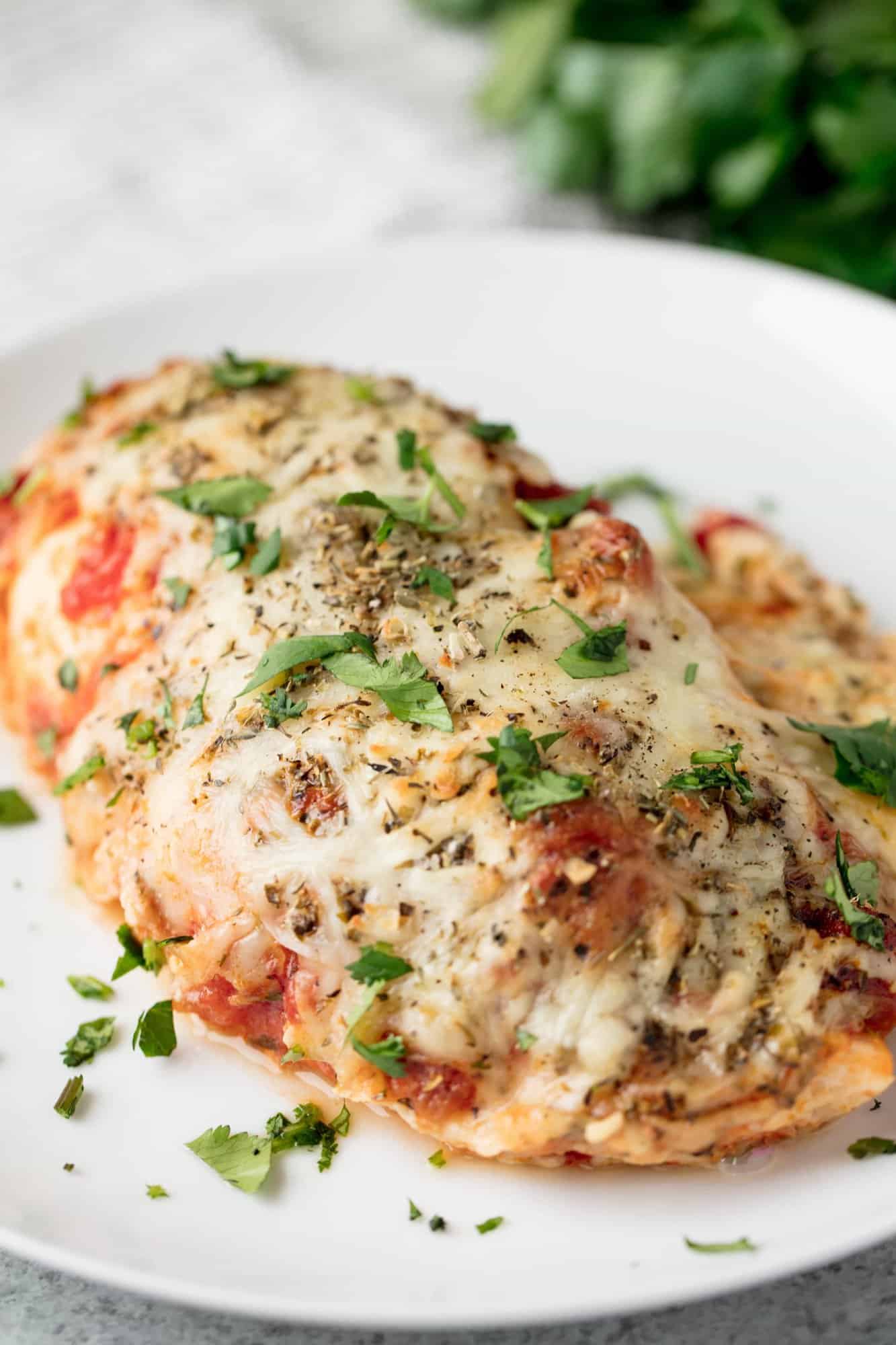 Angled photo of lasagna stuffed chicken breast smothered in cheese and sauce on a red plate.