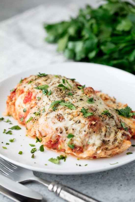 Angled photo of lasagna stuffed chicken breast smothered in cheese and sauce on a red plate.