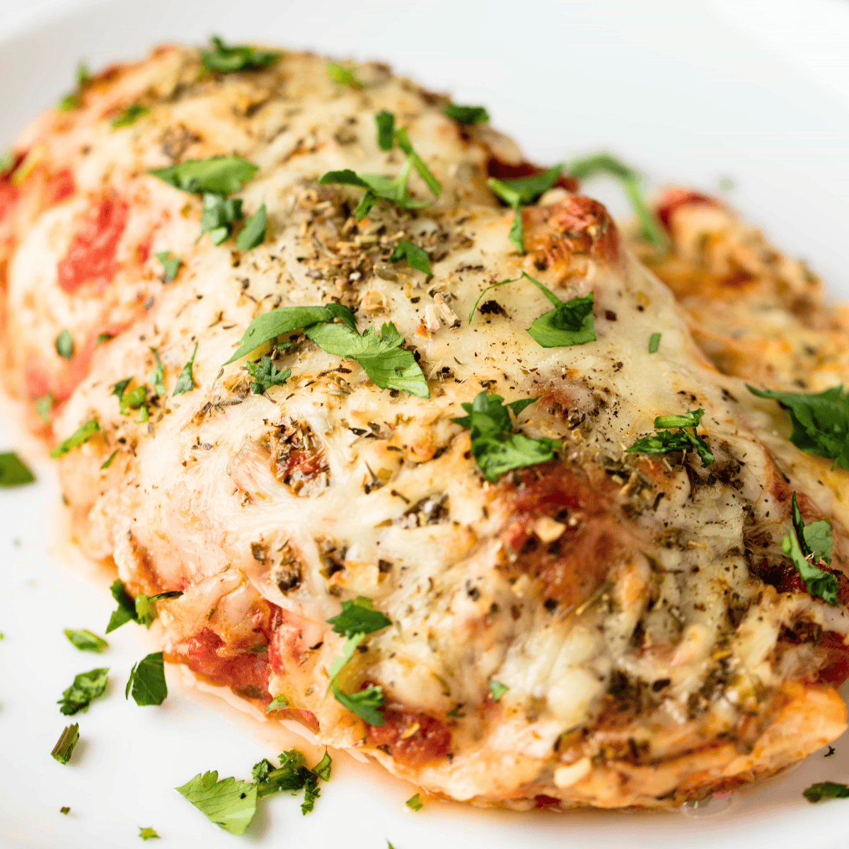 A close up view of a chicken breast that has been stuffed with the flavors of a ricotta lasagna filling and smothered with cheese.