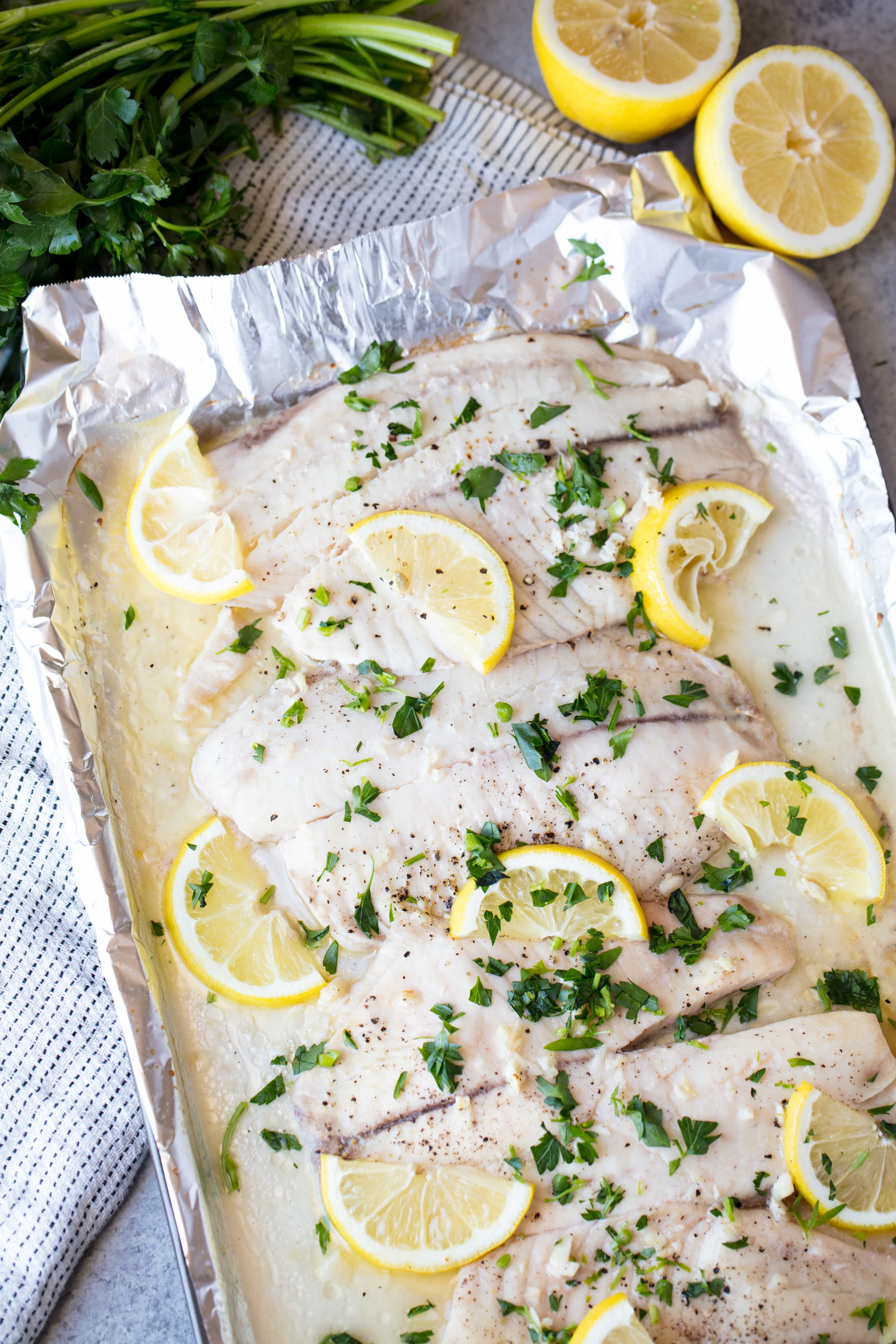 A pan of Baked Tilapia topped with lemon slices and chopped fresh parsley