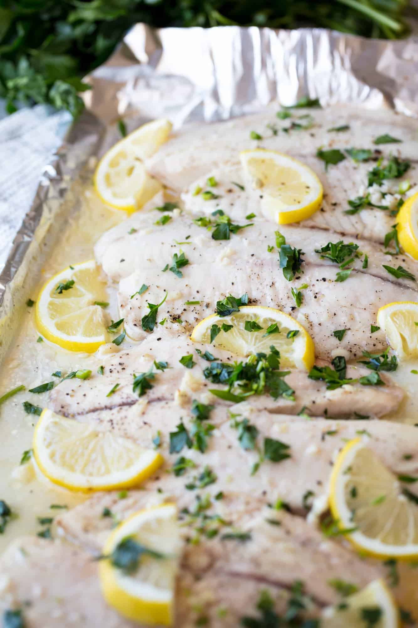 A pan of Baked Tilapia topped with lemon slices and chopped fresh parsley