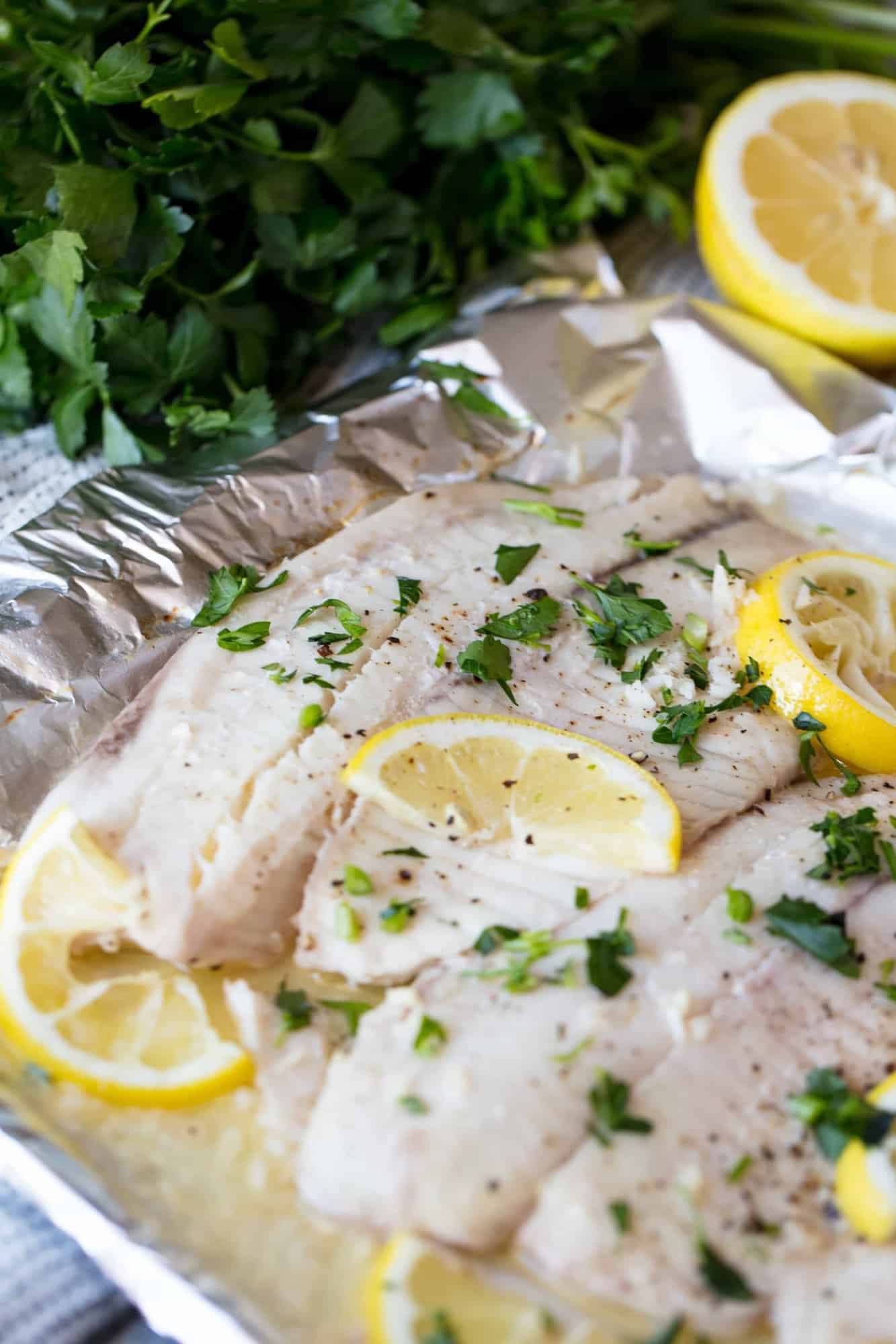 A pan of Baked Tilapia topped with lemon slices and chopped fresh parsley