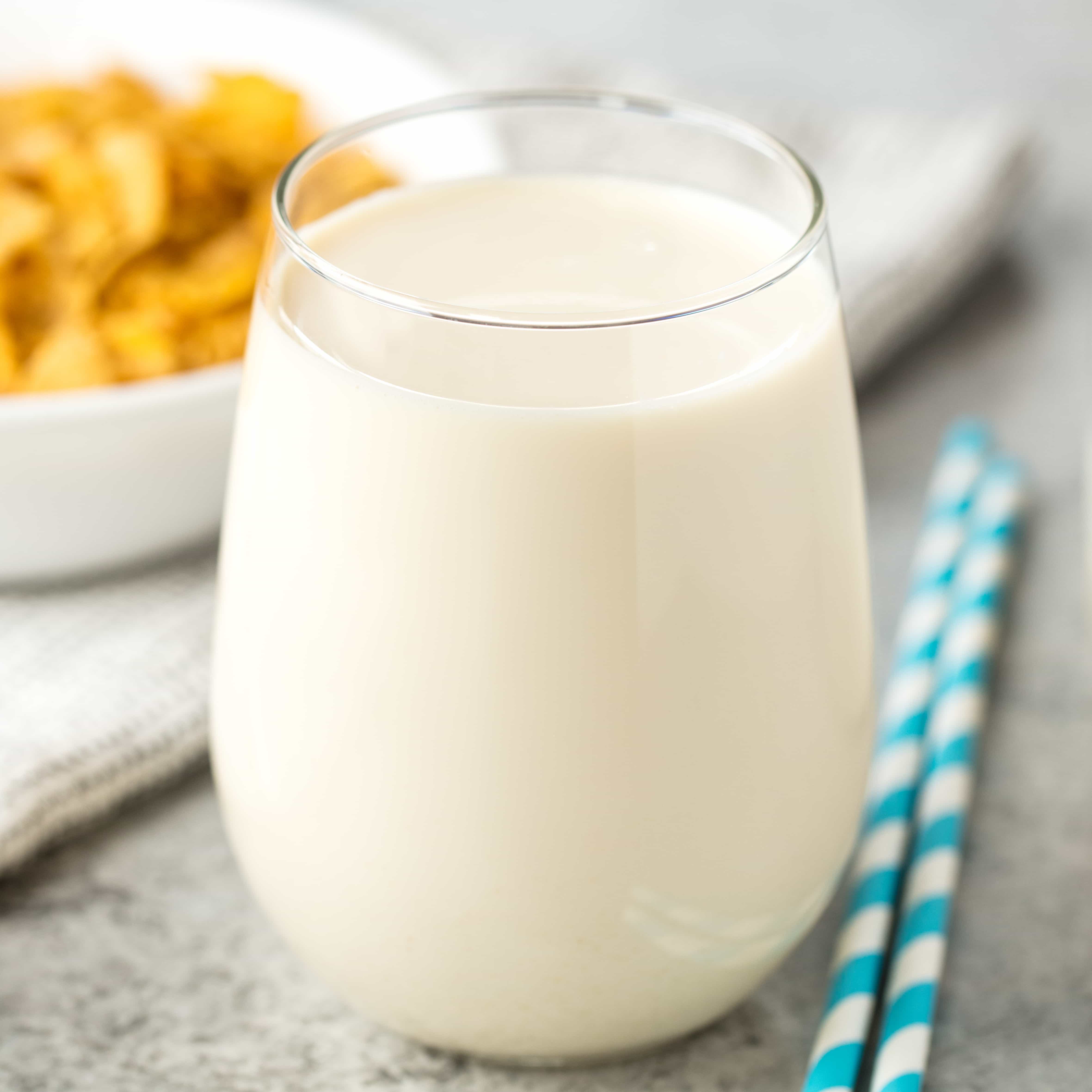 A glass of cereal milk with paper straws resting next to the glass