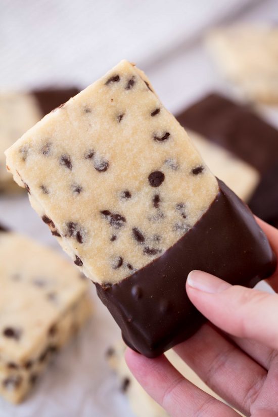 Rachel holds a rectangle shaped chocolate chip shortbread cookie dipped in melted chocolate