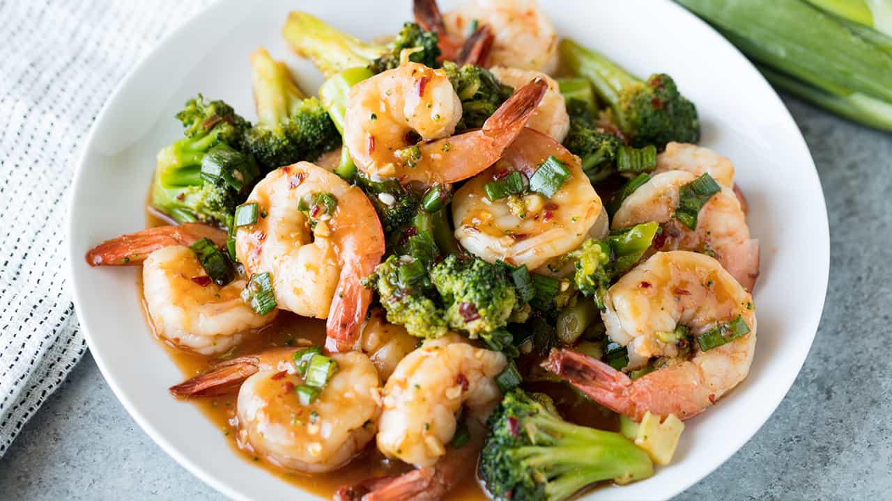Bird's eye view of Szechuan Shrimp and Broccoli in a white serving dish on a concrete countertop.