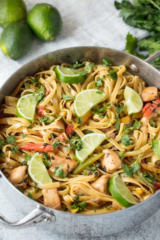 Stainless steel pan with tequila lime chicken pasta in it next to some limes