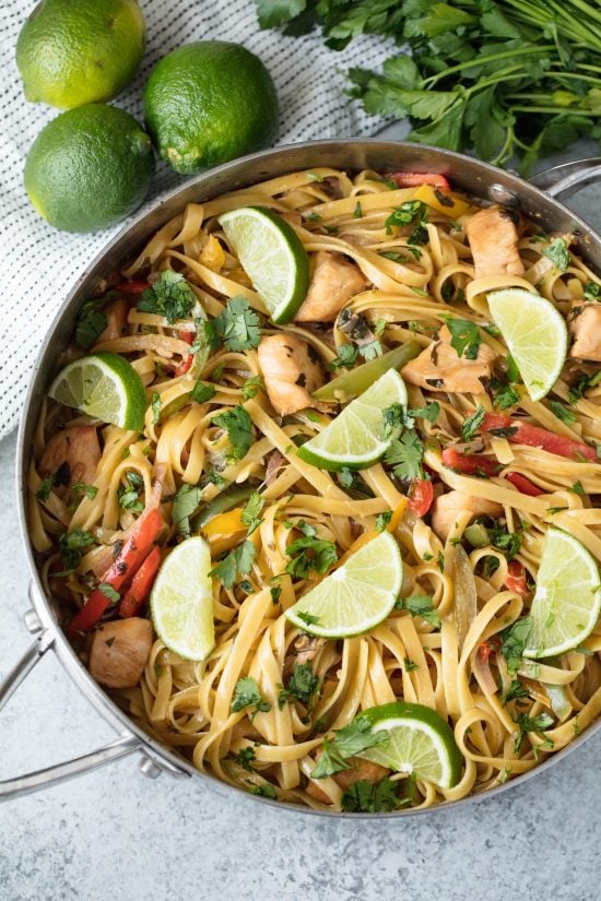 Bird's eye view of a stainless steel pan with tequila lime chicken pasta in it next to some limes