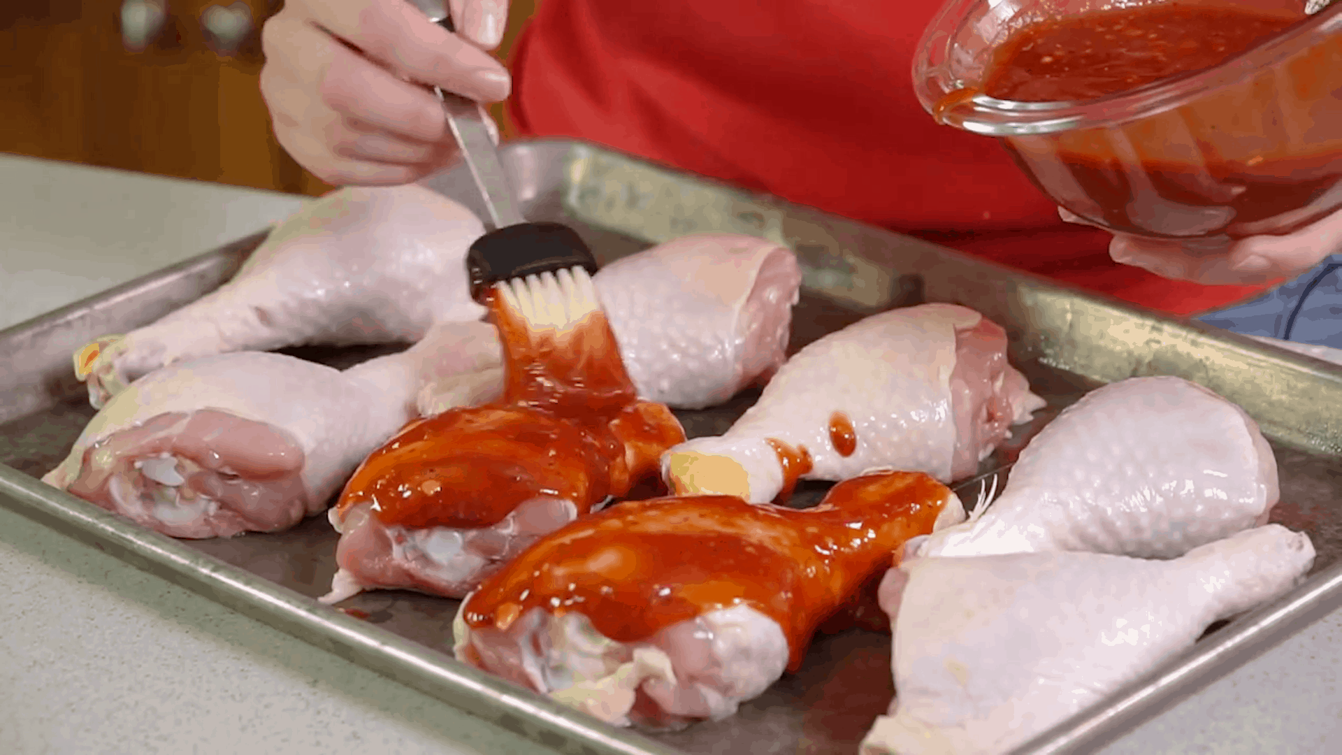 Brushing sauce onto a pan of chicken drumsticks