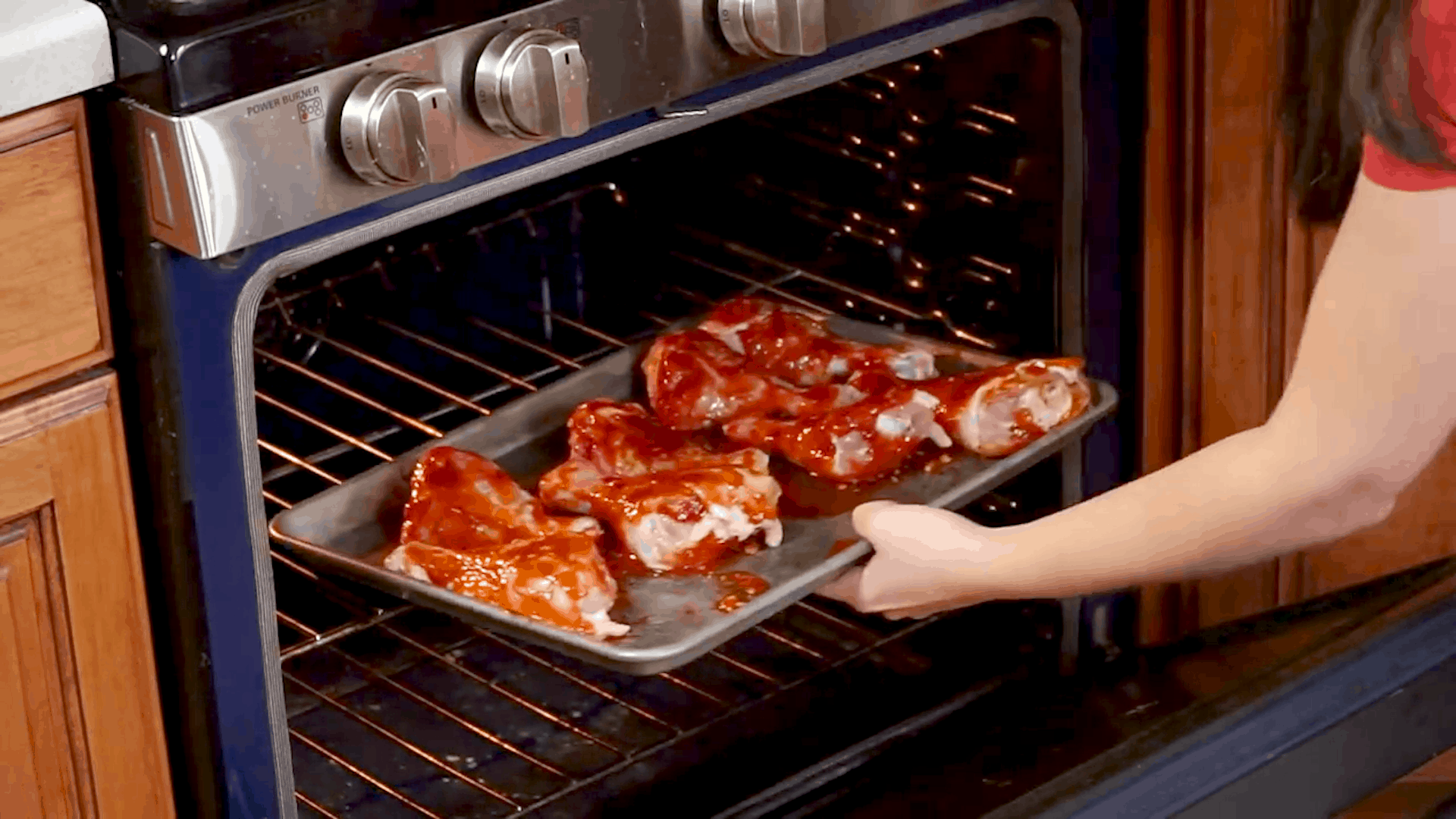 Sheet pan filled with bbq chicken drumsticks being placed into the oven