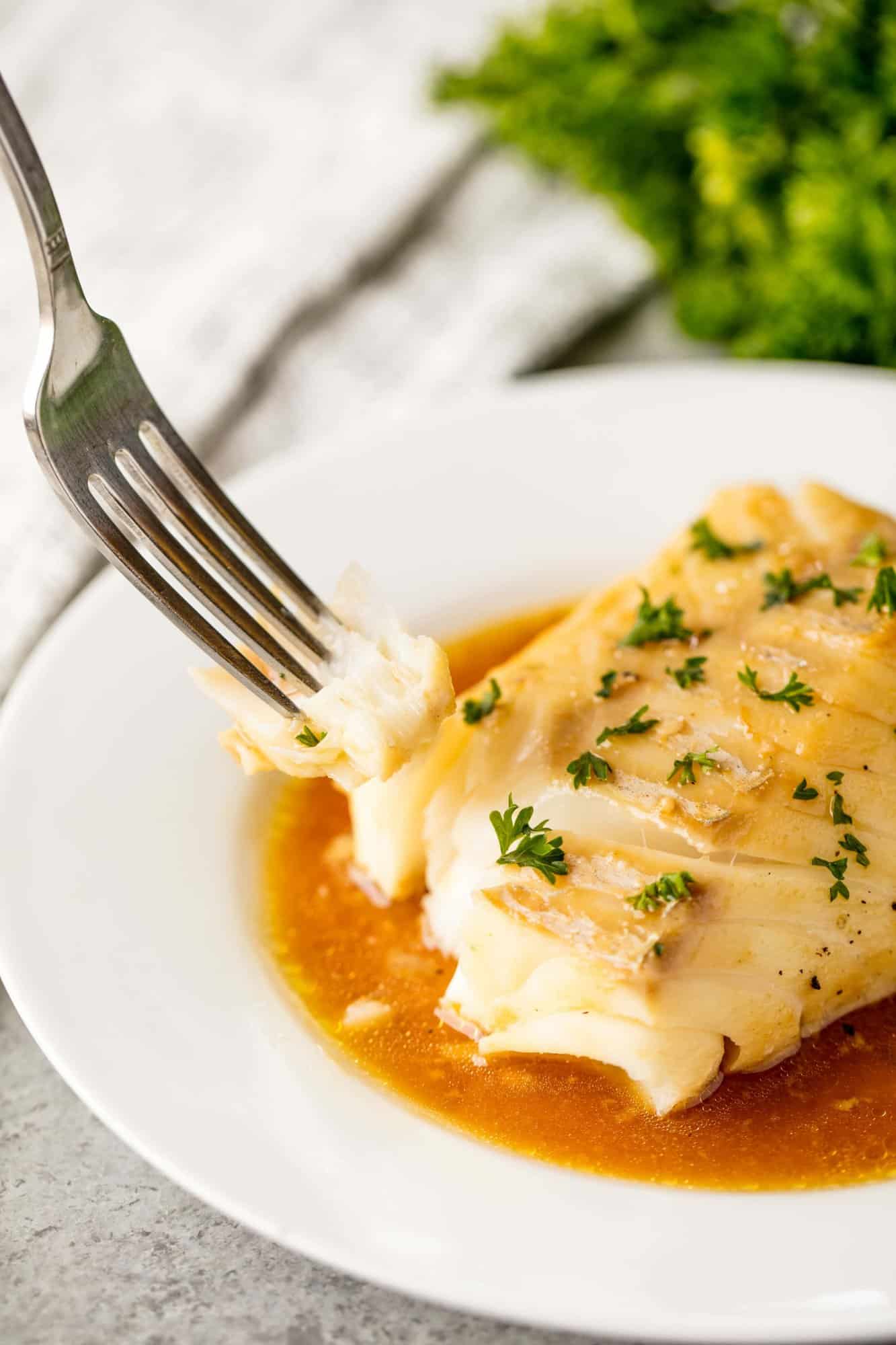 Fork cutting of a bite of ginger glazed baked mahi mahi on a white plate