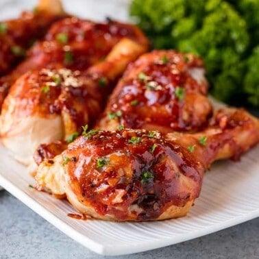 Angled view of Honey Garlic Barbecue Chicken Drumsticks garnished with parsley, lined up on a white serving platter.