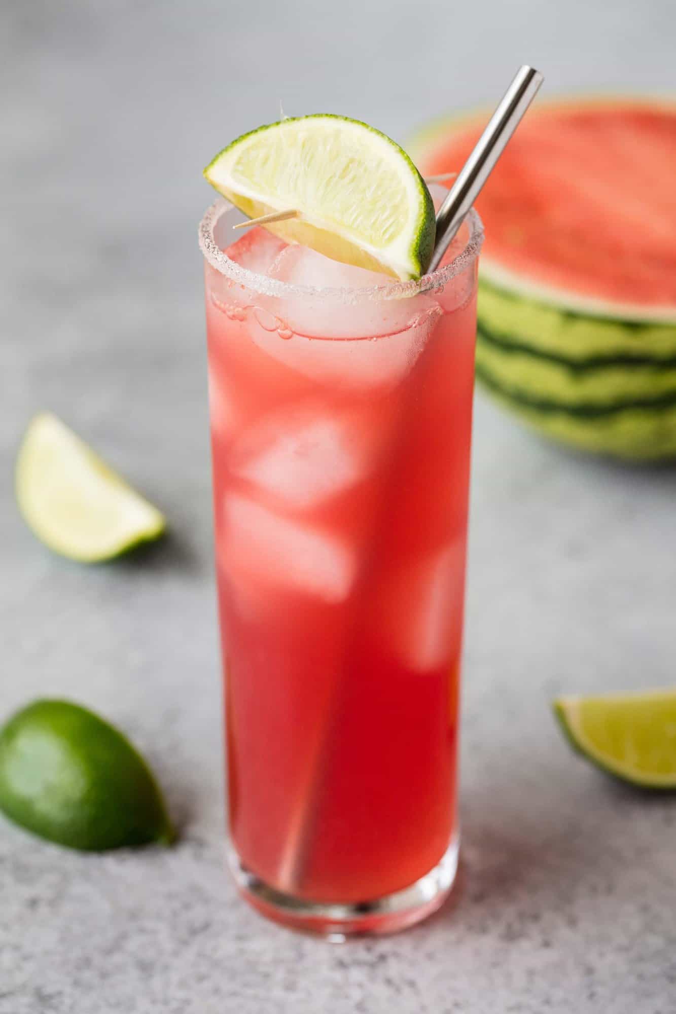 Key west cooler mocktail in a slender glass cup, lip lined with sour sugar, metal straw in cup, and an a lime slice on top.