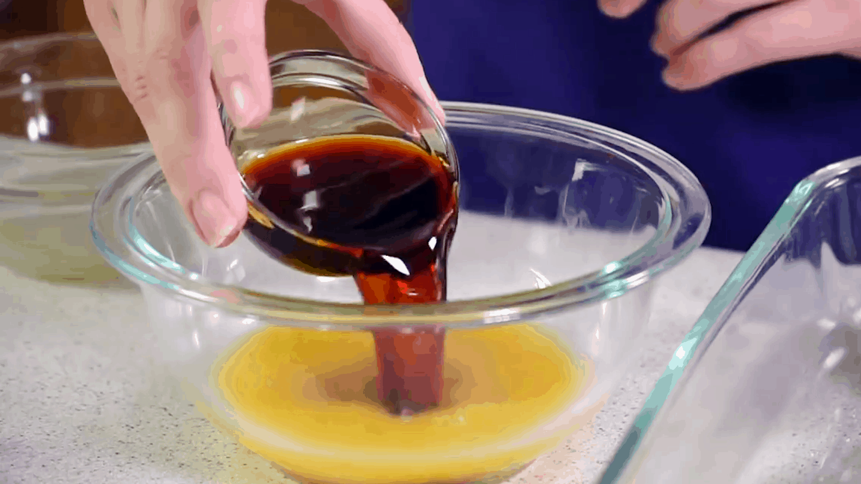 Small glass bowl of soy sauce being poured into a larger glass bowl with orange juice in it