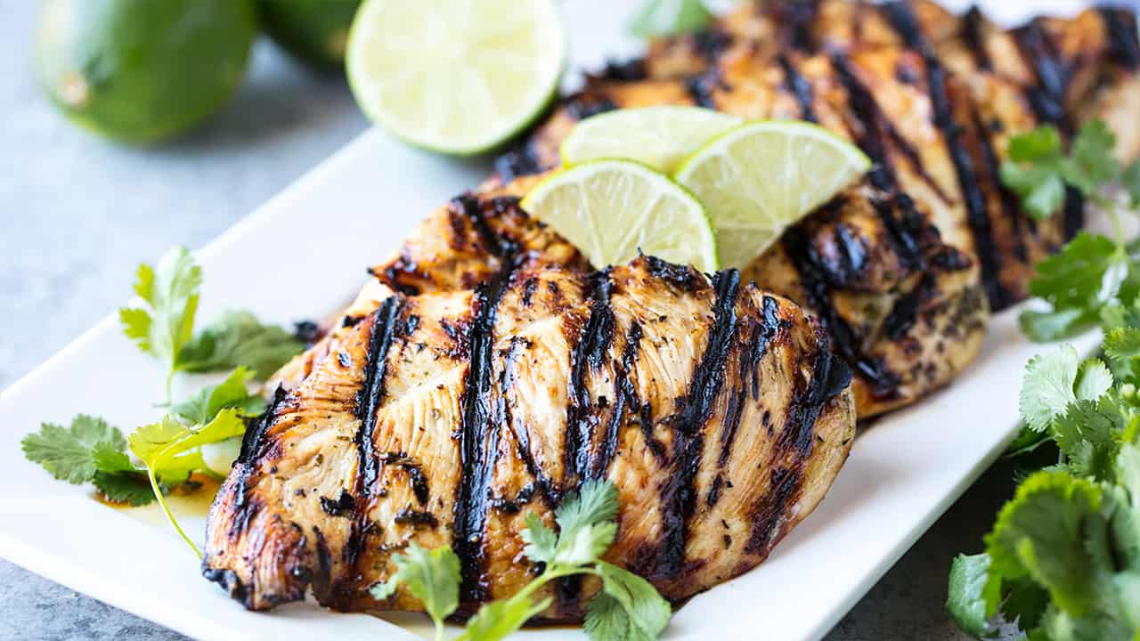 Angled view of Margarita Grilled Chicken garnished with lime slices and cilantro on a white serving platter.