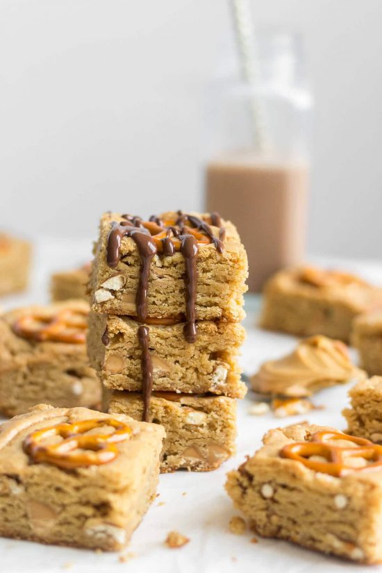 Peanut butter pretzel blondie squares stacked into a pile with chocolate drizzling down the sides