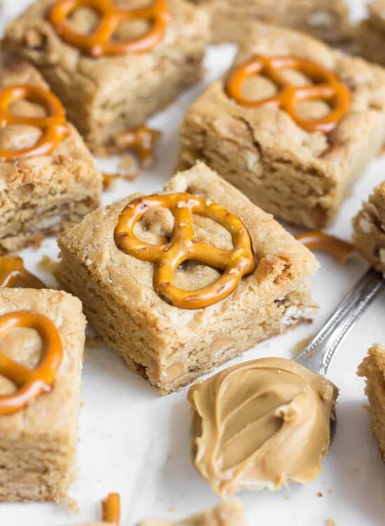 Peanut butter pretzel blondie squares each topped with a pretzel and a spoonful of peanut butter sitting on parchment paper
