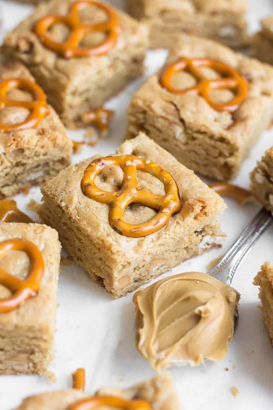 Peanut butter pretzel blondie squares each topped with a pretzel and a spoonful of peanut butter sitting on parchment paper