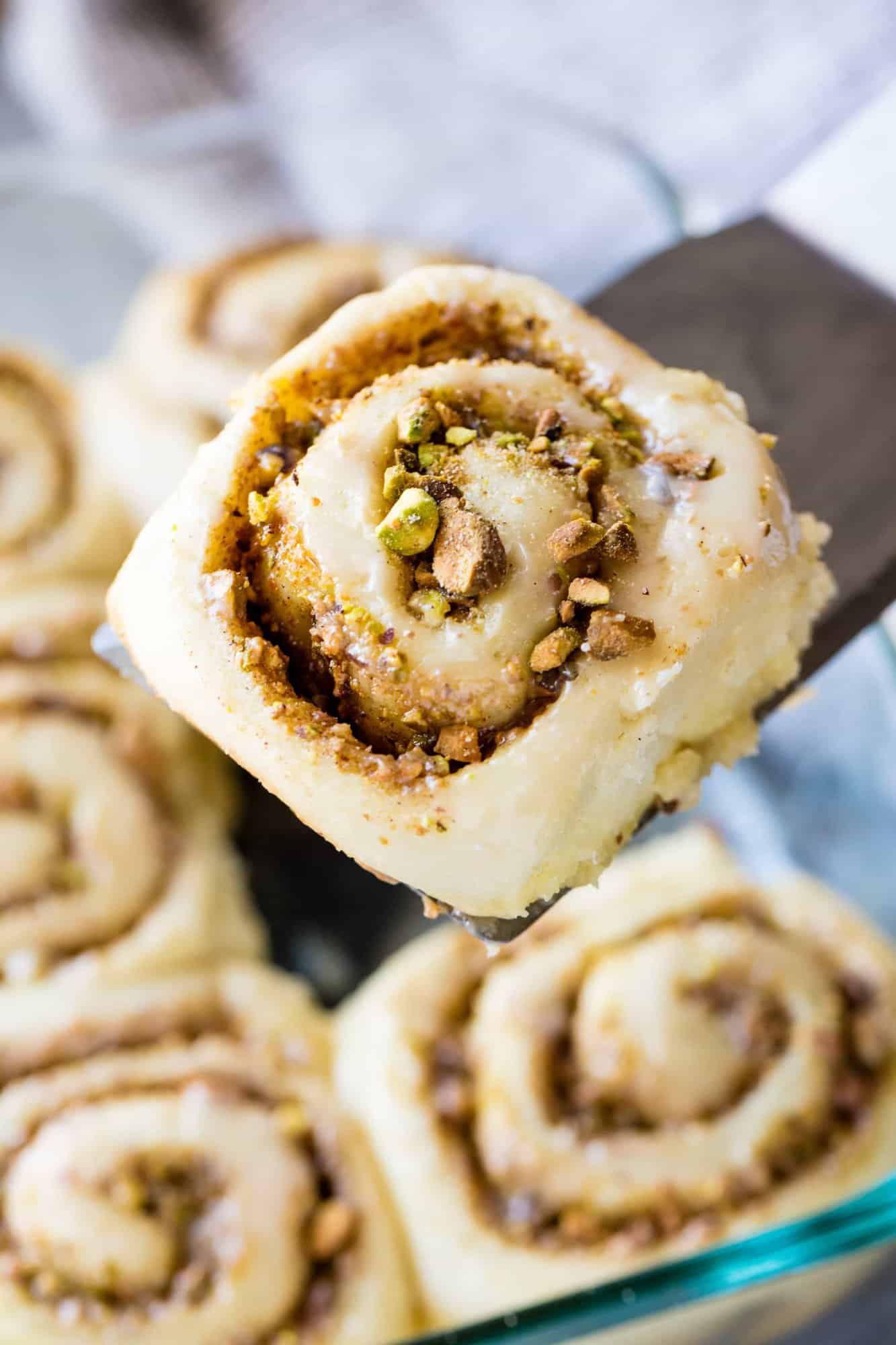 A freshly baked Baklava Cinnamon Roll is lifted from the pan