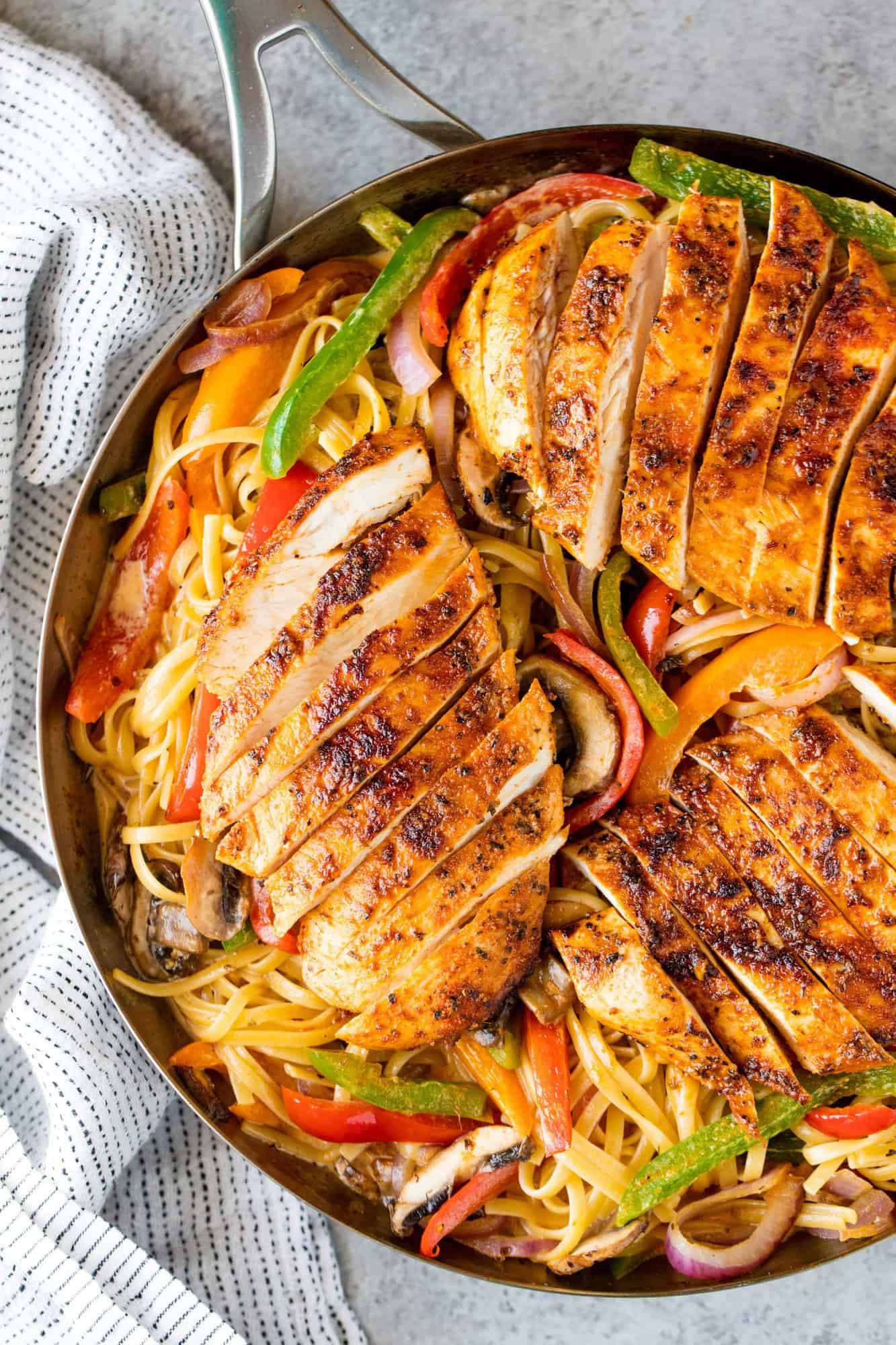 Cajun spiced chicken breasts sliced and served on a bed of linguini with grilled bell peppers, mushrooms and red onion in a skillet