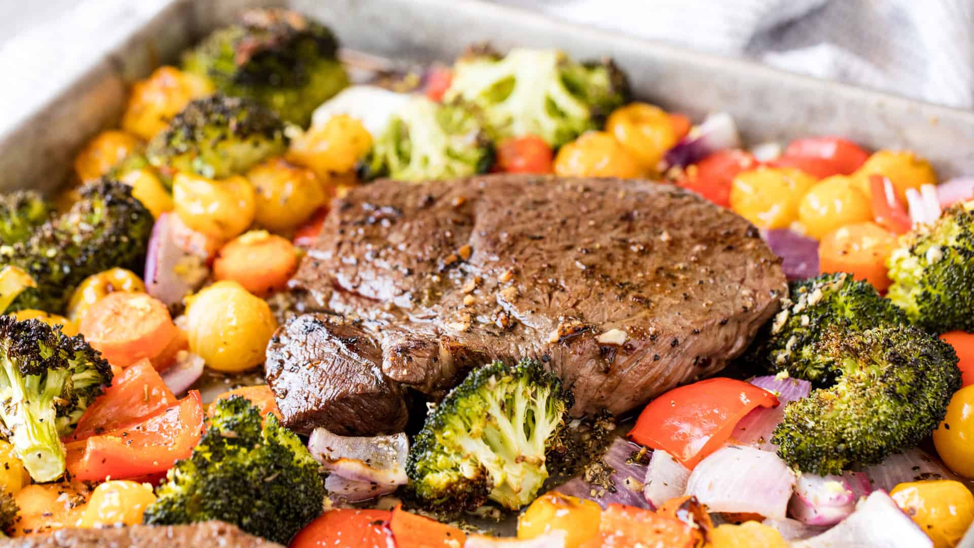 Close up of the steak on a sheet pan full of veggies and the steak..
