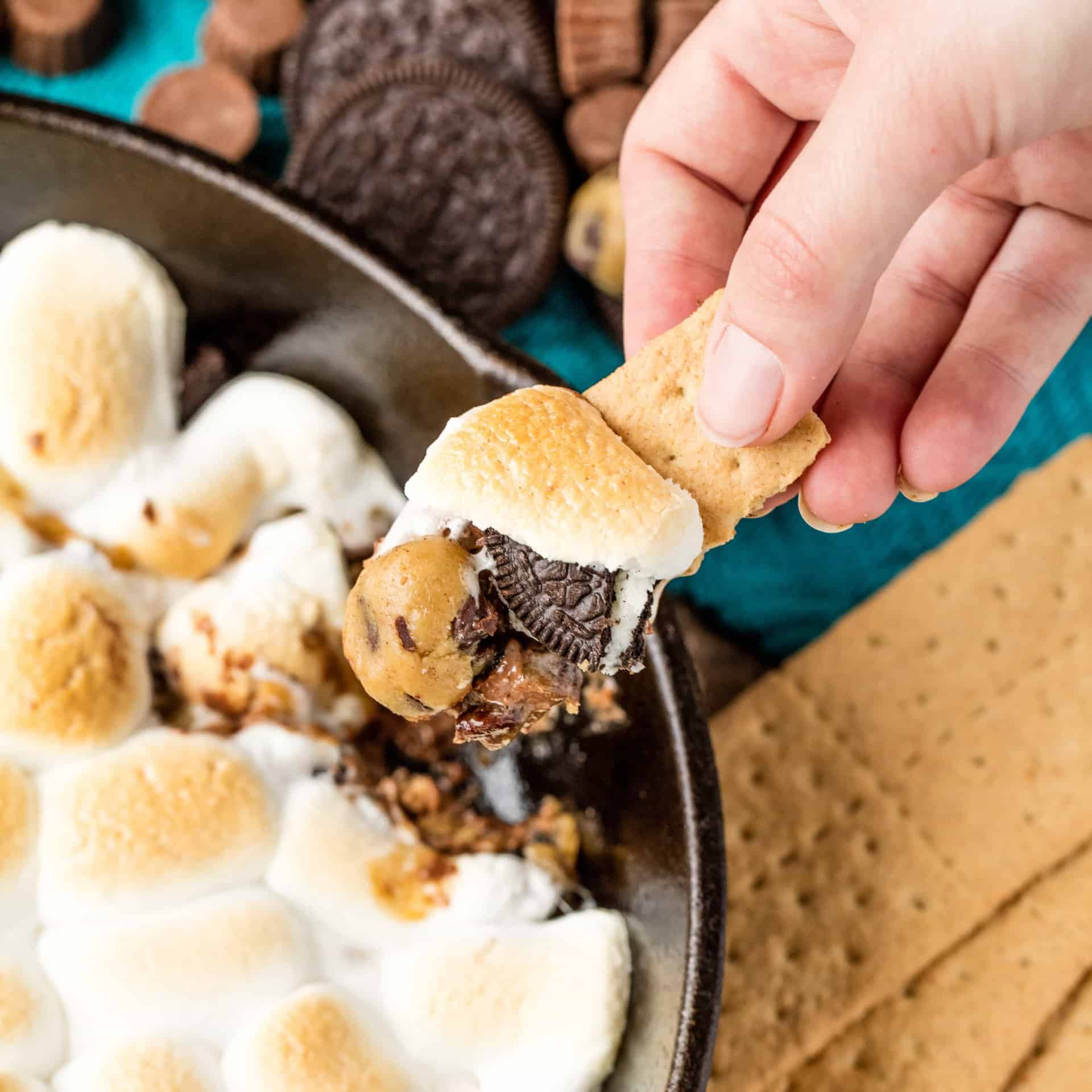 Rachel scoops a bite of million dollar skillet s'mores from a cast iron skillet full of marshmallow, cookie dough, Oreo, and other melty goodness
