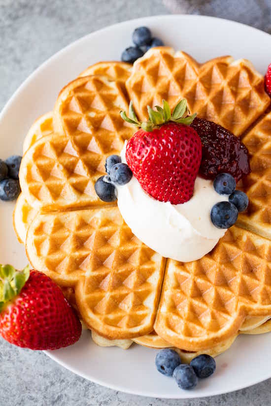 Heart shaped Norwegian waffles on a plate with blueberries, strawberries, crème fraîche, raspberry jam